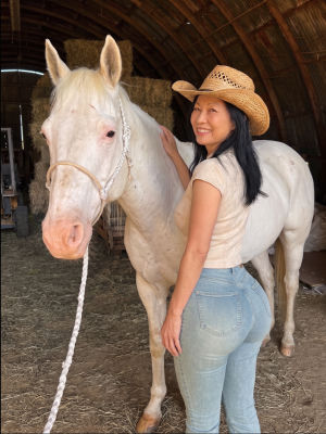 AI generated image of an unidentified woman  posing with a white horse in a barn