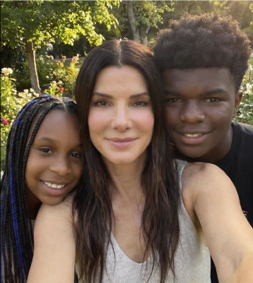 AI-generated selfie-style image of Sandra Bullock with two younger people in a garden