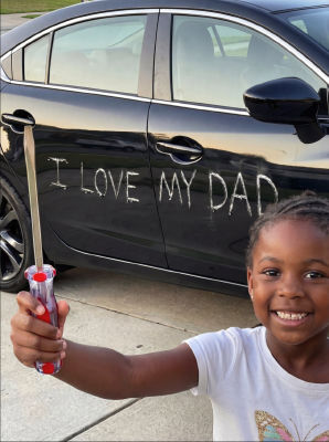 AI-generated image of a child beside a car reading 'I LOVE MY DAD'