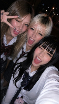 An image showing three young women wearing white collared shirts with patterned ties and bows