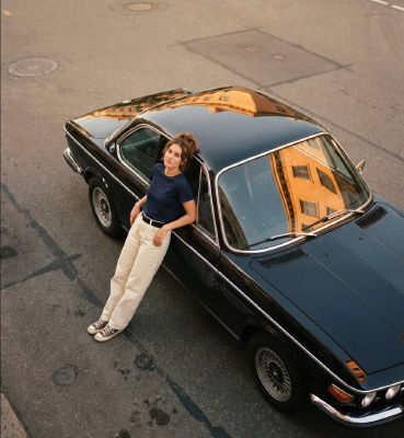 AI-generated image of a woman leaning against a classic car