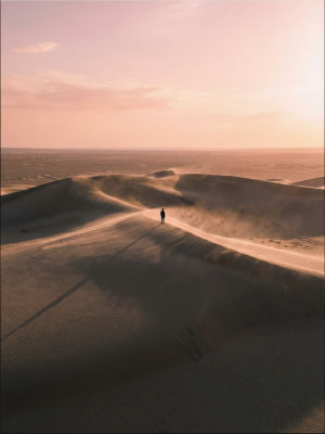 AI-generated image of a lone figure on sand dunes at sunset