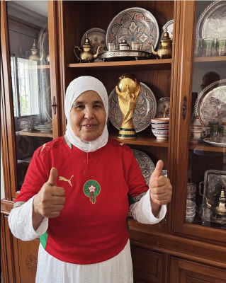 AI-generated image of an elderly woman in a Morocco football jersey beside a World Cup trophy replica