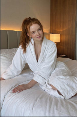 Deepfake of Sadie Sink seated on a hotel bed in a bathrobe