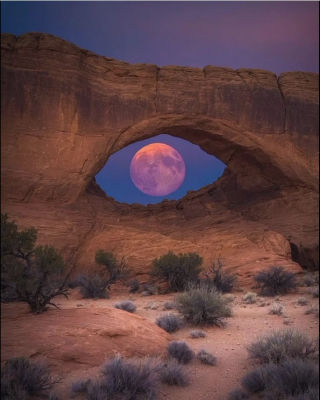 AI-generated image of a full moon framed by a desert sandstone arch at twilight