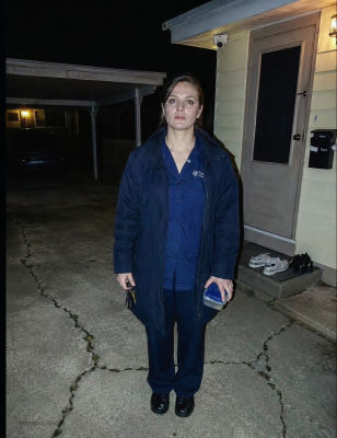 AI-generated image of a woman in scrubs standing outside a house at night